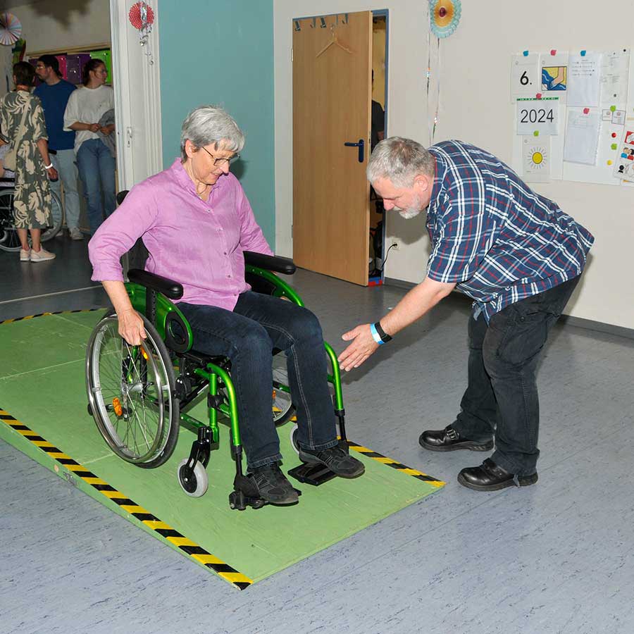 Eine Frau fährt unter Anleitung mit einem Rollstuhl über einen kleinen Parcours.