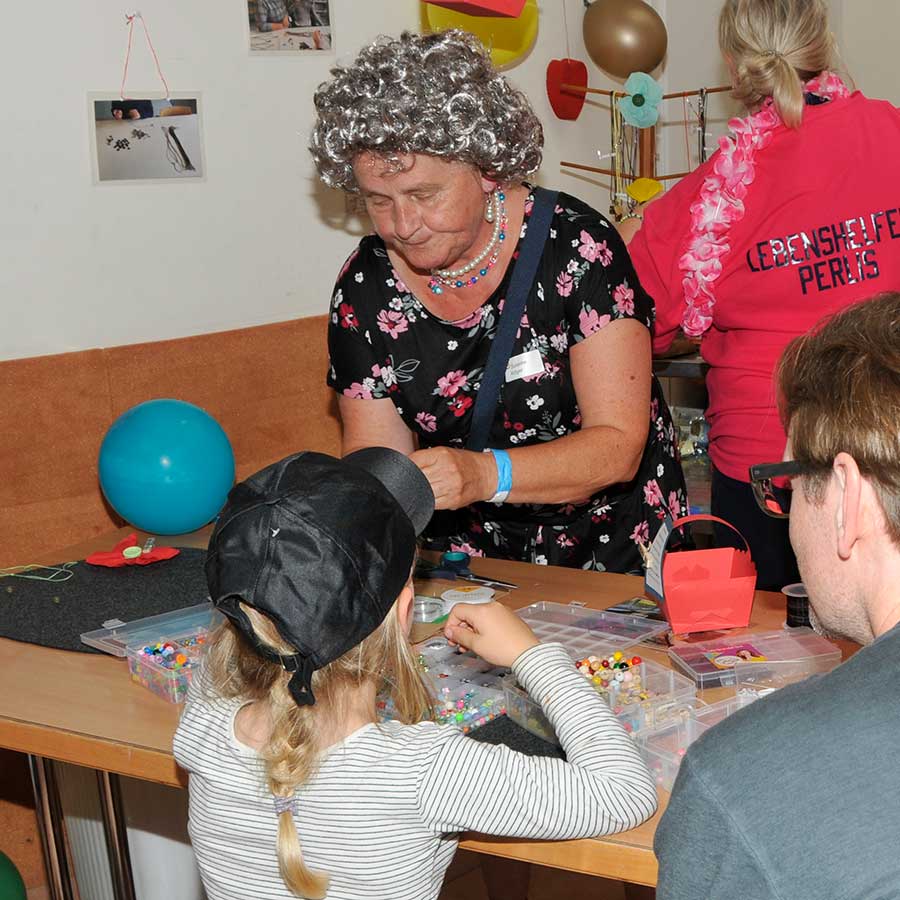 Eine Mädchen sitzt an einem Tisch und stellt unter Anleitung Schmuck aus bunten Perlen her