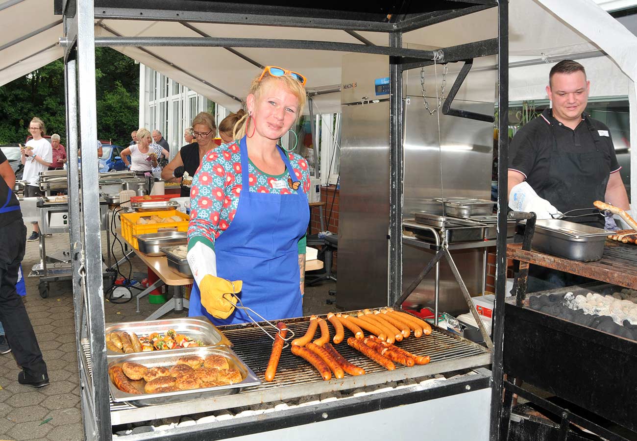 Eine junge Frau grillt Würstchen, Frikadellen und Gemüsespieße.